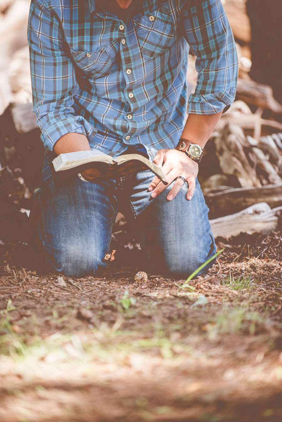 man kneeling on dirt and grass with bible